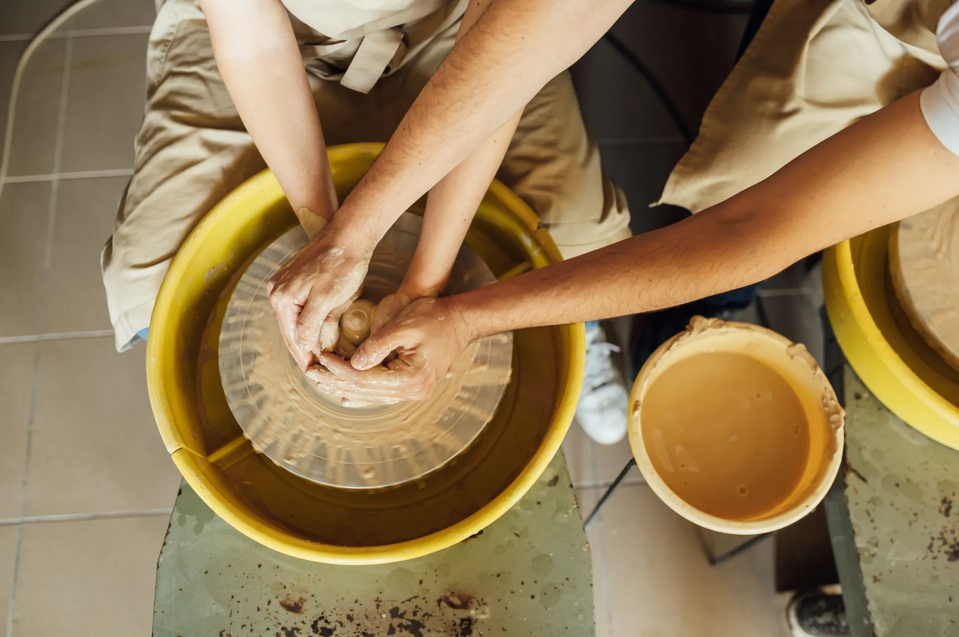 Two people shaping clay together on a pottery wheel