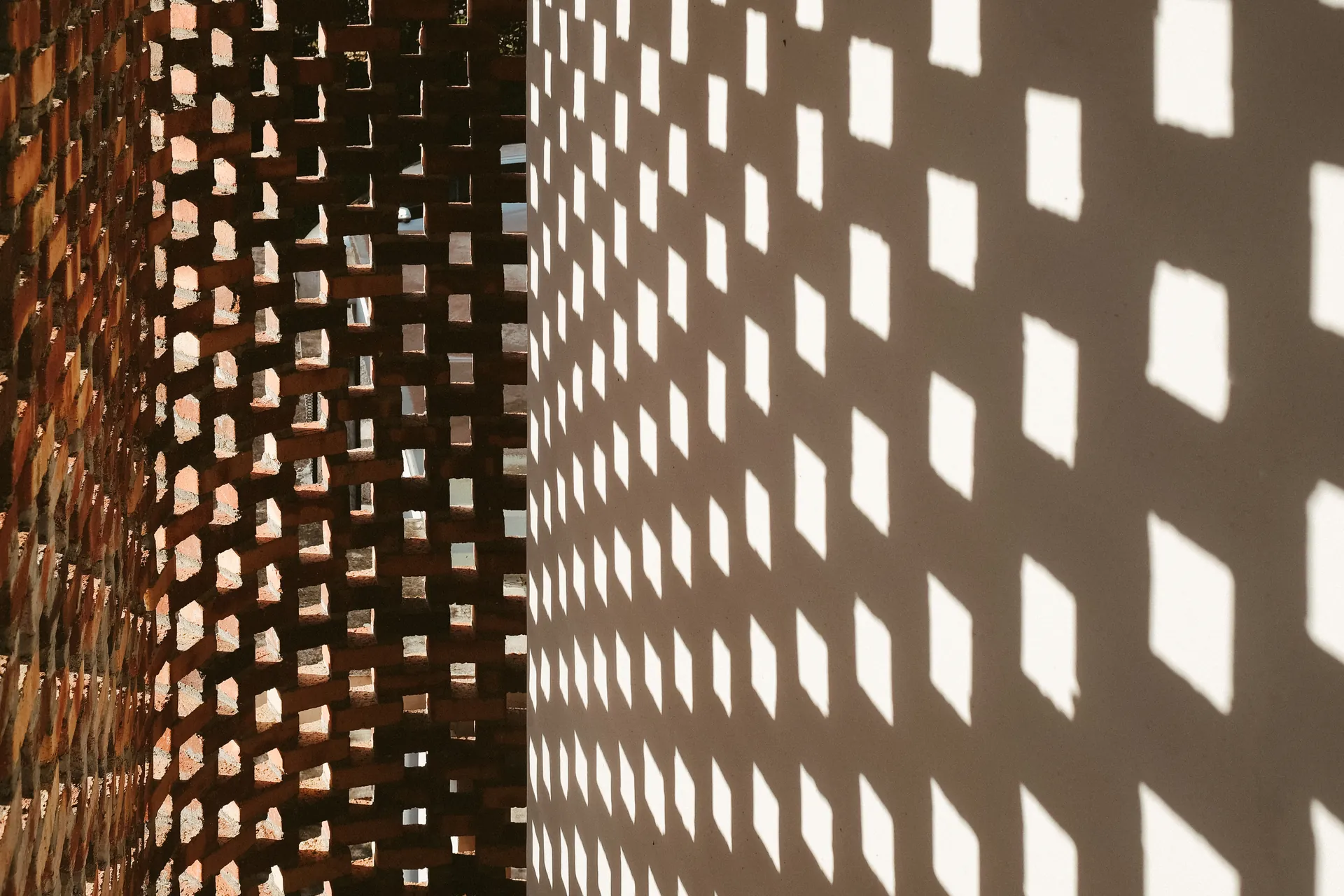 Patterned sunlight passing through an open brick screen onto a wall